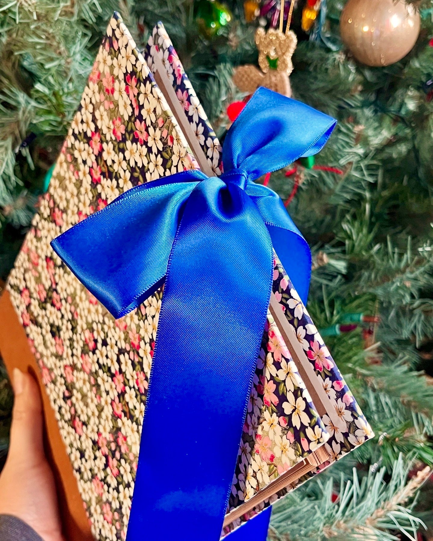 Angled shot of a photo album with a bright blue ribbon tied in a bow, in front of a decorated Christmas tree.