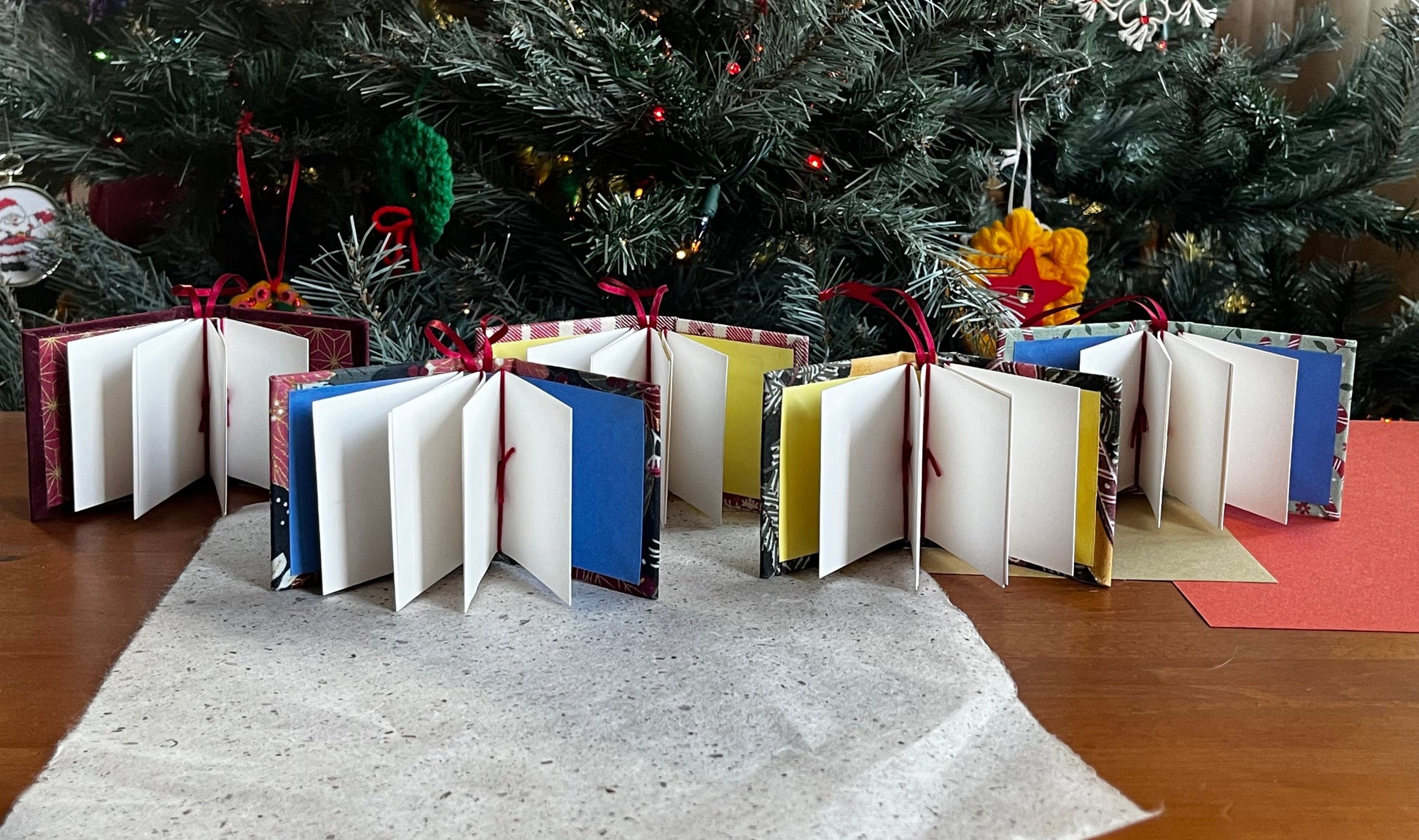 Book shaped christmas ornaments with pages fanned out in front of a christmas tree