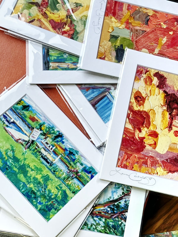 Top down view of a messy pile of matted photo art prints enveloped in clear plastic over a burnt orange flat surface.